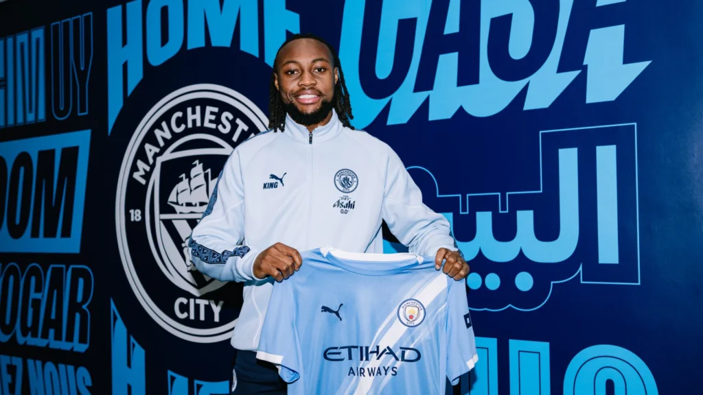 Antoine Semenyo holding up a Manchester City jersey during a media presentation.