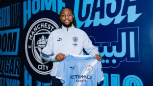 Antoine Semenyo holding up a Manchester City jersey during a media presentation.